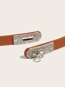 Macro detail of brown pebble leather belt featuring a silver crystal-encrusted turn-lock