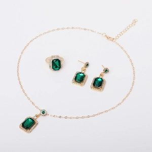 Detail of emerald green rectangular gemstone jewelry set with gold finish on white background