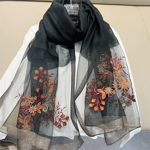 Detailed close-up of intricate floral embroidery on sheer black mesh scarf with gold trims