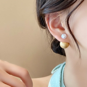 Detailed close-up of matte gold metal and white pearl drop earrings on a model