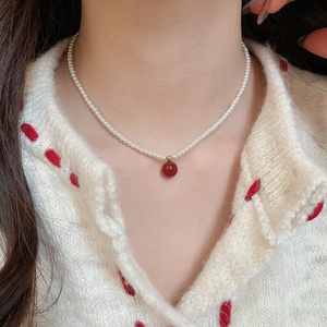 Detailed view of beaded necklace with white pearls and a red gourd tiger eye stone pendant