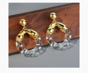 Close-up of twisted glass and gold metal round earrings on a wooden display stand