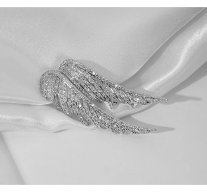 Detail of silver angel wing brooch featuring shimmering inlaid rhinestones on white satin