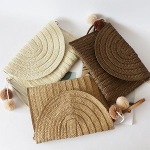 Three straw clutch bags in cream, khaki, and brown with pom-pom charms for beach use