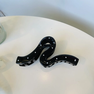 Elegant black hair claw clip with white polka dots on a minimalist white table