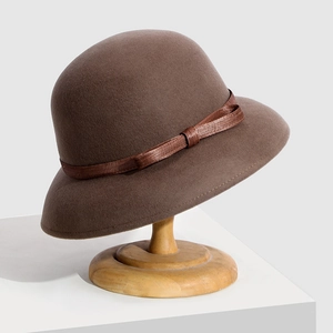 Elegant brown wool felt cloche hat with woven ribbon trim displayed on a wooden stand