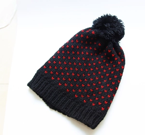 Detail der Winterstrickmütze mit rotem Herzmuster und großem schwarzem Bommel oben
