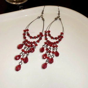 Macro shot of red beaded tassel earrings with faceted crystals on white ceramic plate