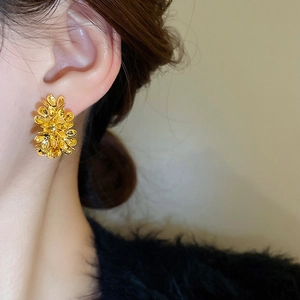 Close-up of golden floral cluster stud earring on a model with a glossy metallic finish