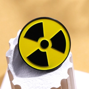 Creative yellow and black radioactive symbol enamel pin on a white textured stone base