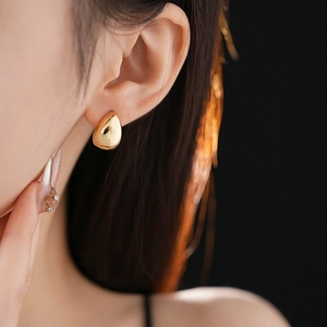 Dettaglio di un orecchino a goccia d'oro minimalista indossato da una modella