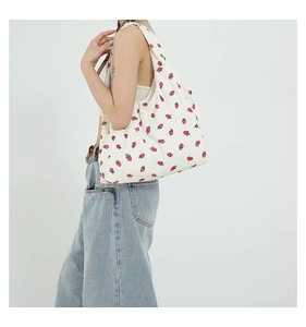 Detail of a large canvas tote bag with red strawberry print shown on model's shoulder