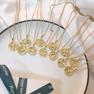 Golden 18K zodiac necklaces with embossed coin pendants on white silk background