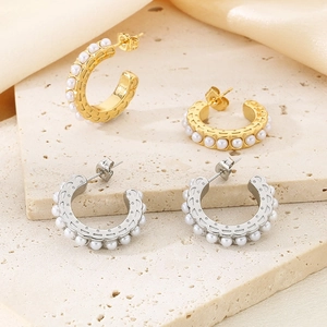 Macro detail of gold and silver C-shaped earrings with pearls on textured stone