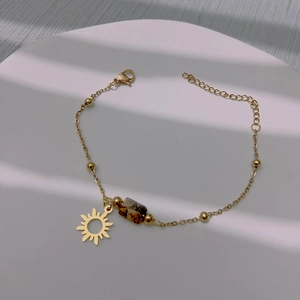 Gold sun charm bracelet with marble stone beads on a minimalist white textured display