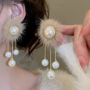 Detail of plush pom pom earrings with white pearls and long golden fringe tassels