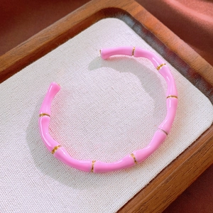 Dettaglio del bracciale rigido rosa stile bambù con anelli dorati su supporto bianco
