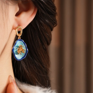 Detail view of vintage flower earrings with blue petals and golden metallic texture on a model