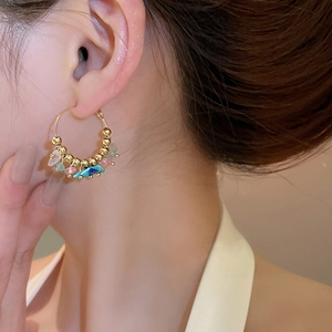 Close-up of bohemian hoop earring featuring colorful crushed stones and golden beads