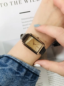 Detail of a rectangular gold quartz watch with a brown leather strap on a model's wrist