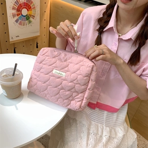 Pink quilted heart cosmetic bag with zipper held by a model in a lifestyle setting