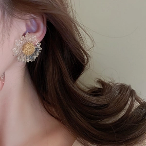 Detail of transparent daisy flower earrings with gold center worn by a model