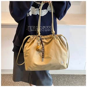 Detail view of khaki drawstring tote bag featuring braided knot pendant and floral logo