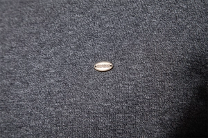 Close-up of dark grey knitted sweater fabric with brand logo metal plate detail