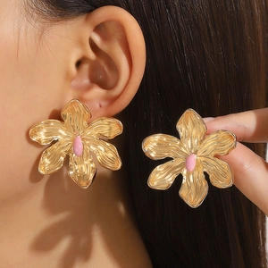 Close-up of a large golden flower earring featuring a pink center and rippled petals