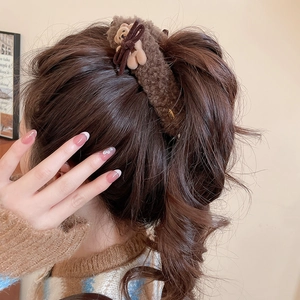 Close-up of brown plush bear hair clip with bow decoration worn on hair for styling