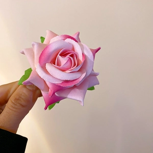 Detailed view of handmade pink fabric rose hair clip with green leaves and layers