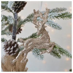 Champagne gold glitter elk ornament hanging on snowy Christmas tree branch with bokeh