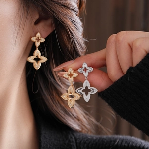 Detail of long drop earrings with double gold four-leaf flowers and white cubic zirconia
