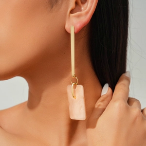 Close-up of elegant long geometric earrings with gold metal and pink marble resin texture