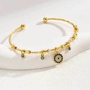 Adjustable gold evil eye bangle with blue zircon charms and textured finish on a white stand