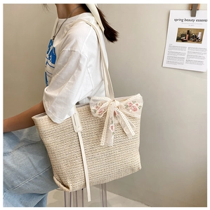Straw woven tote bag with lace flower bow detail shown on shoulder in a lifestyle setting