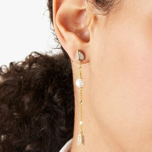 Detail of a gold heart stud earring with hanging pearl and arrow charm on model