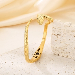 Makroaufnahme des goldenen Schlangenarmreifs mit Schuppentextur auf Stein und Seide