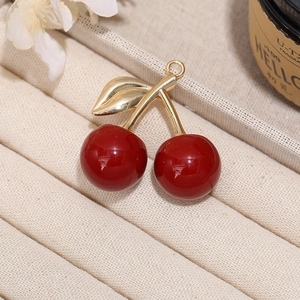 Macro shot of gold-plated cherry pendant charm with glossy red finish on jewelry tray