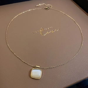Détail macro du collier en titane doré avec pendentif carré blanc en œil-de-chat
