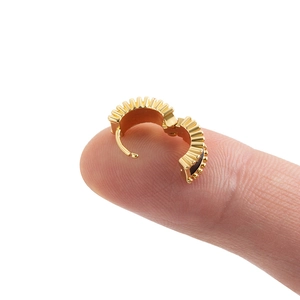 Mini gold huggie hoop earring with textured scallop design held on a fingertip