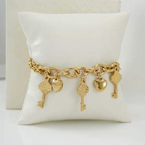 Detail shot of a golden charm bracelet with vintage keys and hearts on a white pillow