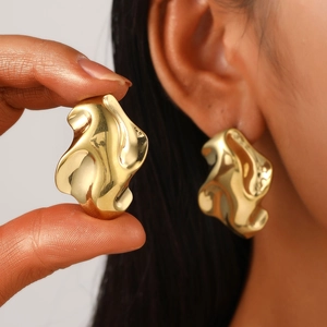Close-up of golden irregular wavy stud earrings with polished mirror finish on ear