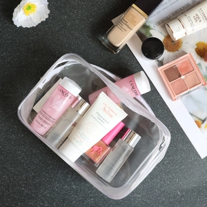 Transparent PVC makeup bag with white zipper shown with cosmetics on a textured table