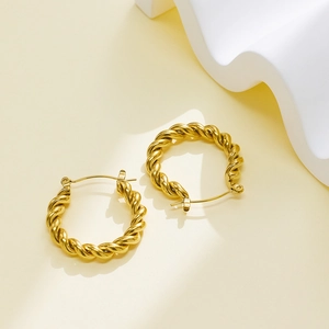 Détails de boucles d'oreilles créoles torsadées en acier inoxydable doré sur fond beige
