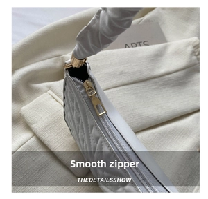 Detail of smooth gold zipper and white quilted texture on luxury cloud handbag