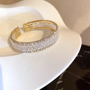 Close-up of golden open bangle with layered clear beads and sparkling crystal trim