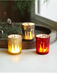 Three festive Christmas glass candle holders in gold, black, and red on a wood base