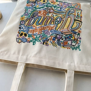 Close-up of colorful embroidery pattern on a beige canvas tote bag with hand-drawn art