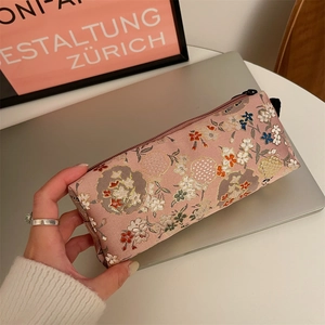 Pink floral embroidery stationery case with zipper closure and side handle shown in hand